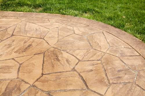 picture of a curved beige stamped concrete patio or slab with grass