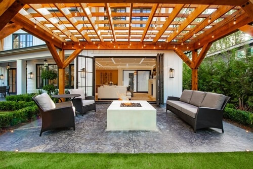 backyard concrete patio with seating and overhead wooden gazebo with hanging lights